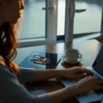 A woman working on her laptop in front of a window.