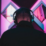 A man wearing headphones in front of a pink background.