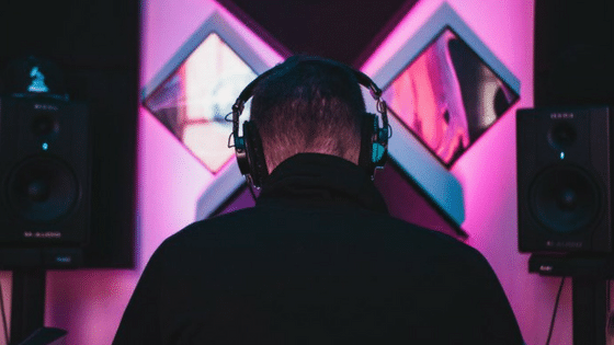 A man wearing headphones in front of a pink background.