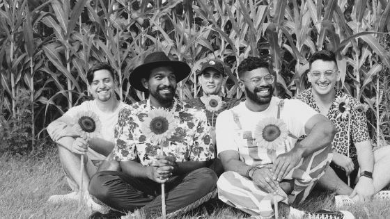 A black and white photo of a group of men sitting in front of a corn field.