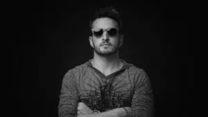 A man in sunglasses standing in front of a black background.