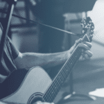 A man playing an acoustic guitar in front of a microphone.