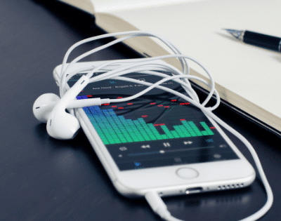 A white phone next to a notebook and earphones.