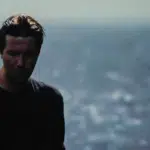 A man in a black shirt standing in front of a city.