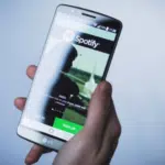 A person holding up a phone with spotify on it.