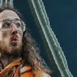 A man with glasses and a beard standing in front of a cactus.