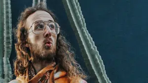 A man with glasses and a beard standing in front of a cactus.