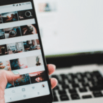 A person holding a cell phone in front of a laptop.