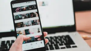 A person holding a cell phone in front of a laptop.