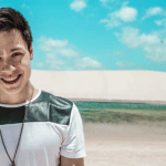 A young man smiling in front of a sand dune.