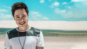 A young man smiling in front of a sand dune.