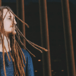 A man with dreadlocks standing in front of a fence.