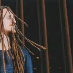 A man with dreadlocks standing in front of a fence.