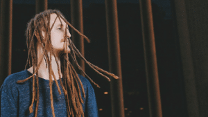 A man with dreadlocks standing in front of a fence.