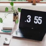 A laptop on a desk with a clock on it.