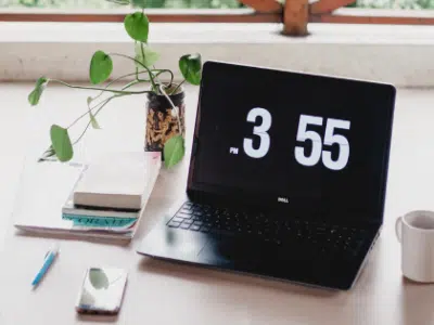 A laptop on a desk with a clock on it.