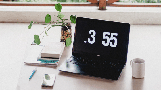 A laptop on a desk with a clock on it.