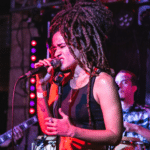 A woman with dreadlocks singing into a microphone.