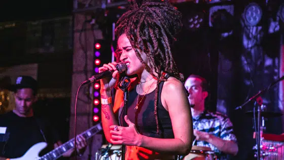 A woman with dreadlocks singing into a microphone.