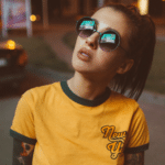 A woman wearing sunglasses and a yellow ringer t - shirt.