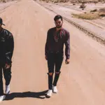 Two men walking down a dirt road in the desert.