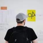 A man with a backpack looking at a wall of paper.