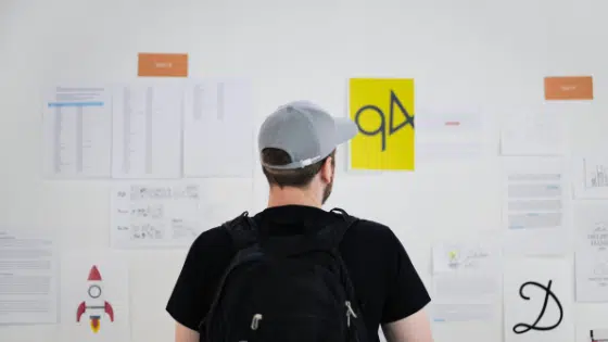 A man with a backpack looking at a wall of paper.