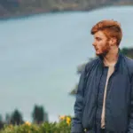 A man standing on a hill overlooking a lake.