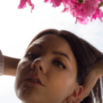 A woman is posing in front of a pink flower.