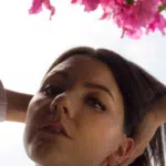 A woman is posing in front of a pink flower.