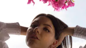 A woman is posing in front of a pink flower.