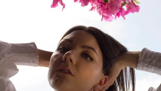 A woman is posing in front of a pink flower.