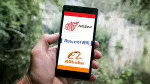 A person holding a cell phone with a tencent and alibaba logo on it.