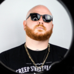 A man with a red beard and sunglasses in front of a mirror.