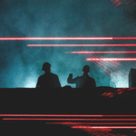 Two djs on stage with red lights behind them.