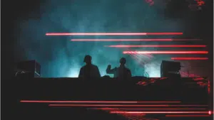 Two djs on stage with red lights behind them.