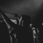 A black and white photo of people raising their hands at a concert.