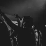 A black and white photo of people raising their hands at a concert.