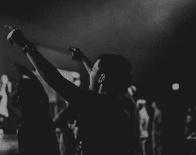 A black and white photo of people raising their hands at a concert.