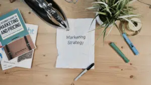 A notepad with the word marketing strategy on it sits on a wooden table.