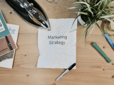 A notepad with the word marketing strategy on it sits on a wooden table.