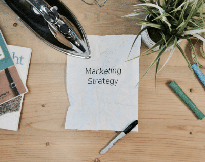 A notepad with the word marketing strategy on it sits on a wooden table.