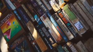A collection of old, worn paperback books arranged in rows, some stacked, with visible creases and faded covers in various colors.