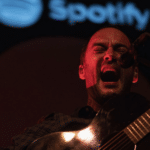 A man playing an acoustic guitar in front of a spotify logo.