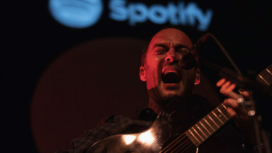 A man playing an acoustic guitar in front of a spotify logo.