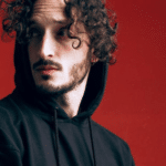 A man in a black hoodie with curly hair.