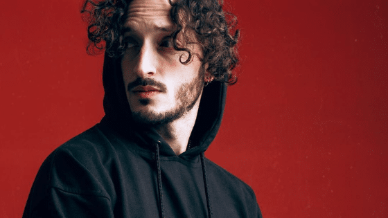 A man in a black hoodie with curly hair.