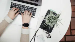 A woman typing on a laptop on a white table.