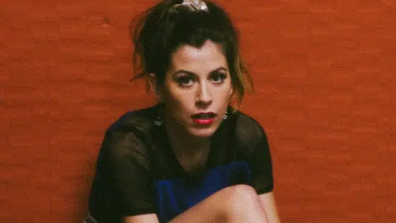 A woman in a blue dress sitting on a red wall.