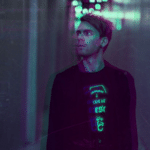 A man standing in a hallway with neon lights.